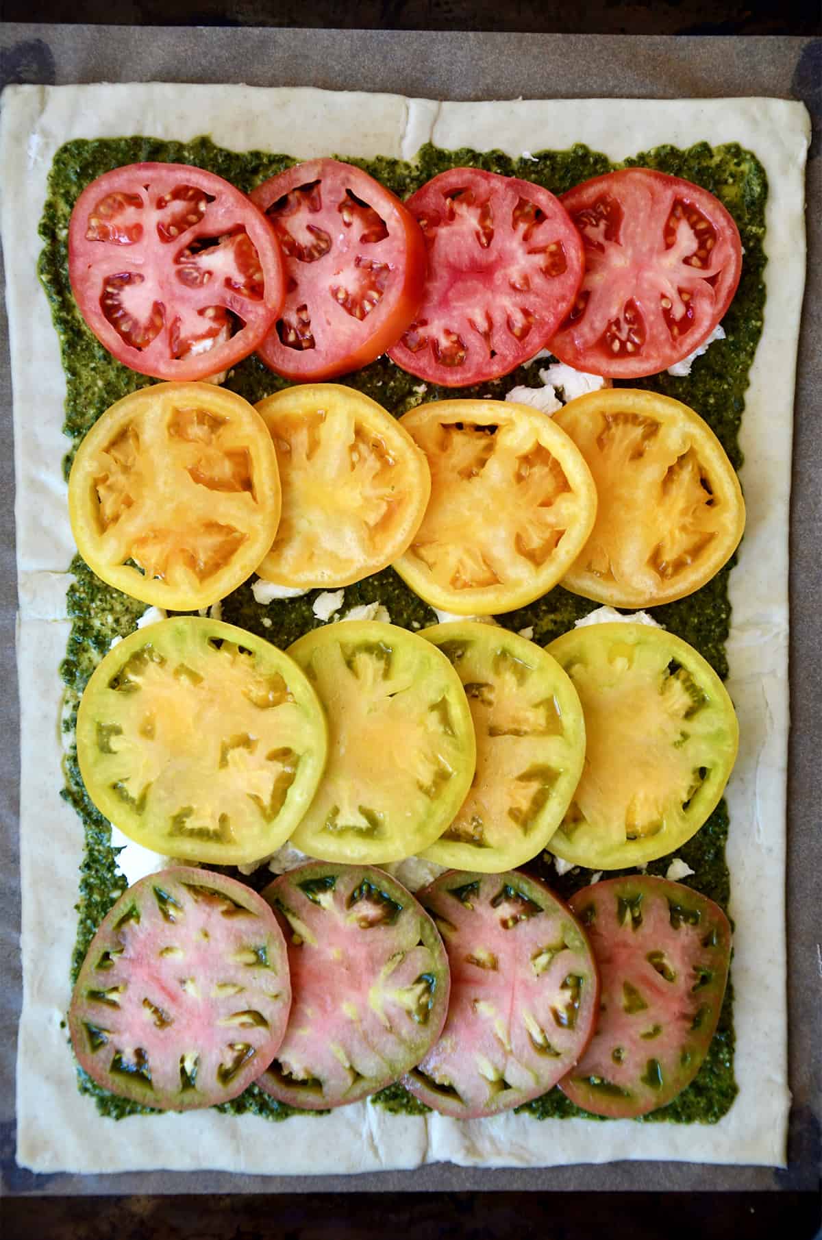 A rectangle of puff pastry topped with pesto, crumbled goat cheese and sliced tomatoes.