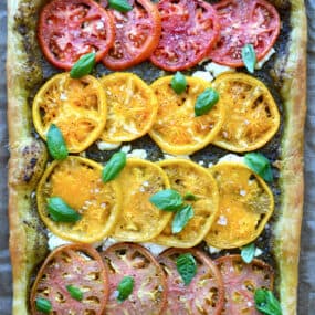 A baked tomato and goat cheese tart topped with small basil leaves.