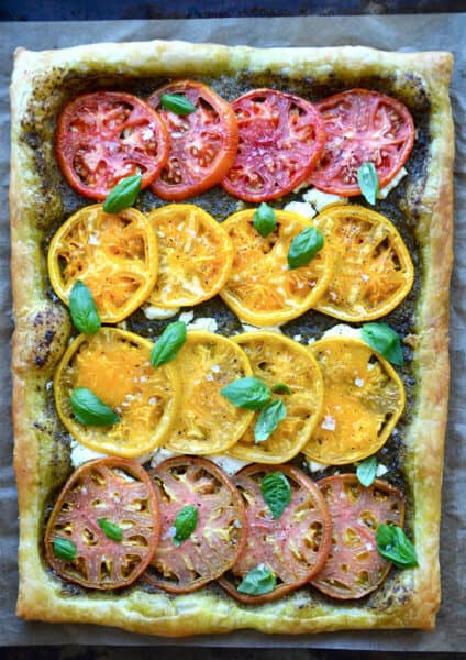 A baked tomato and goat cheese tart topped with small basil leaves.