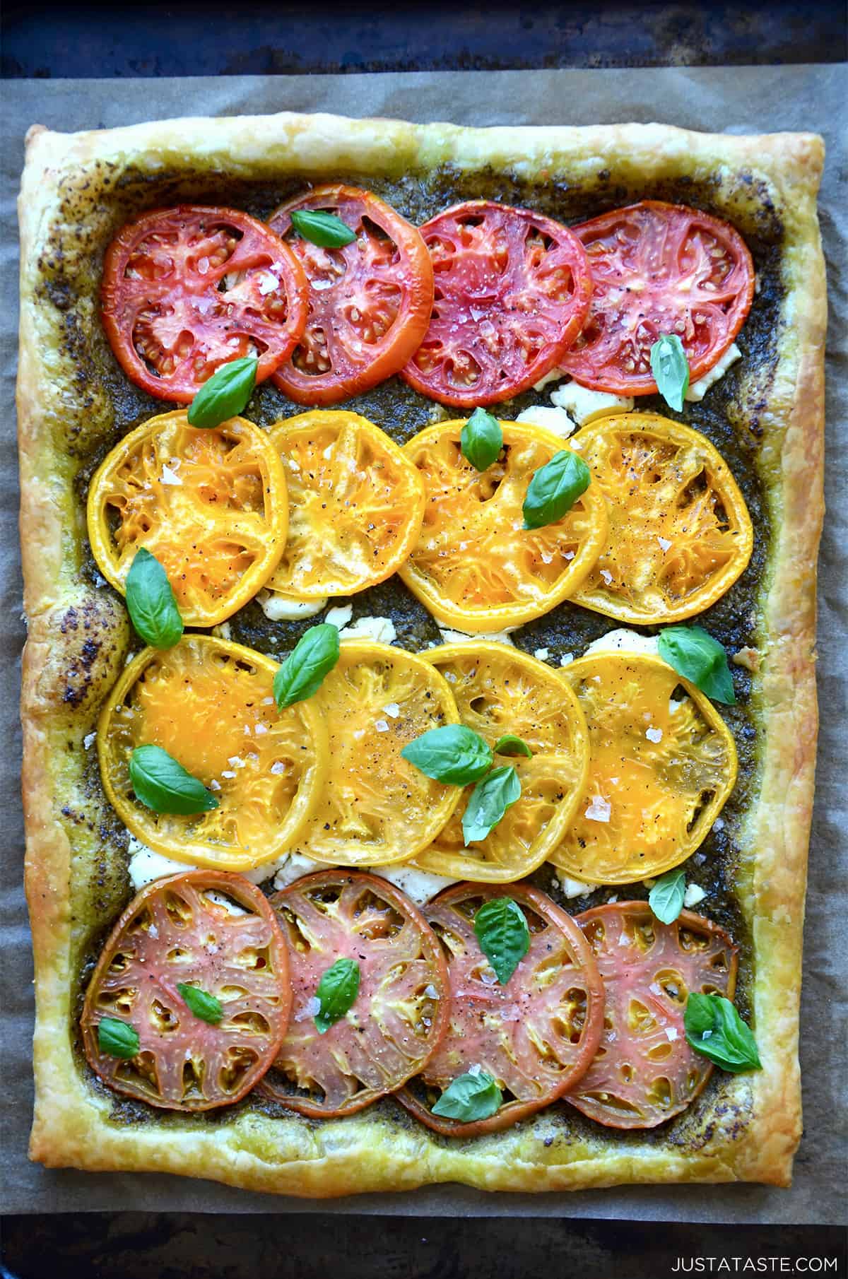 A baked tomato and goat cheese tart topped with small basil leaves.