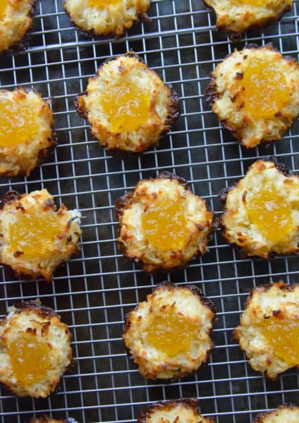 Coconut macaroons filled with pineapple jam are arranged in rows on a cooling rack.
