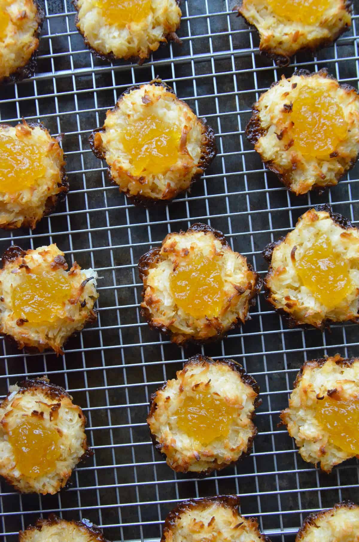 Coconut macaroons filled with pineapple jam are arranged in rows on a cooling rack.