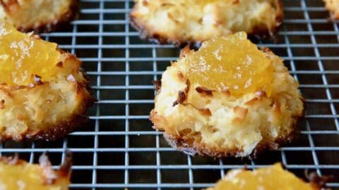 Coconut macaroons filled with pineapple jam are arranged in rows on a cooling rack.