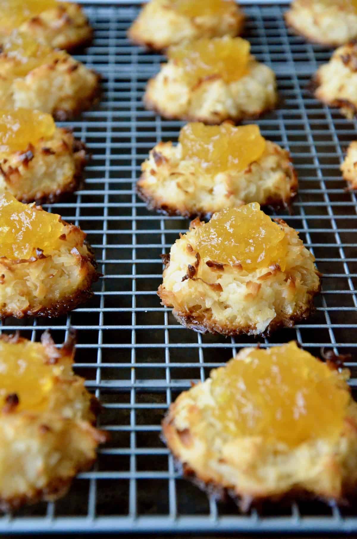 Coconut macaroons filled with pineapple jam are arranged in rows on a cooling rack.