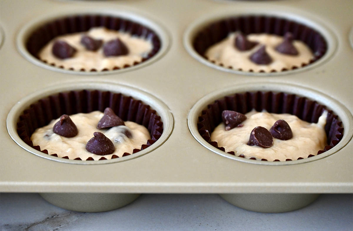 Unbaked banana bread muffins topped with chocolate chips in a muffin pan.