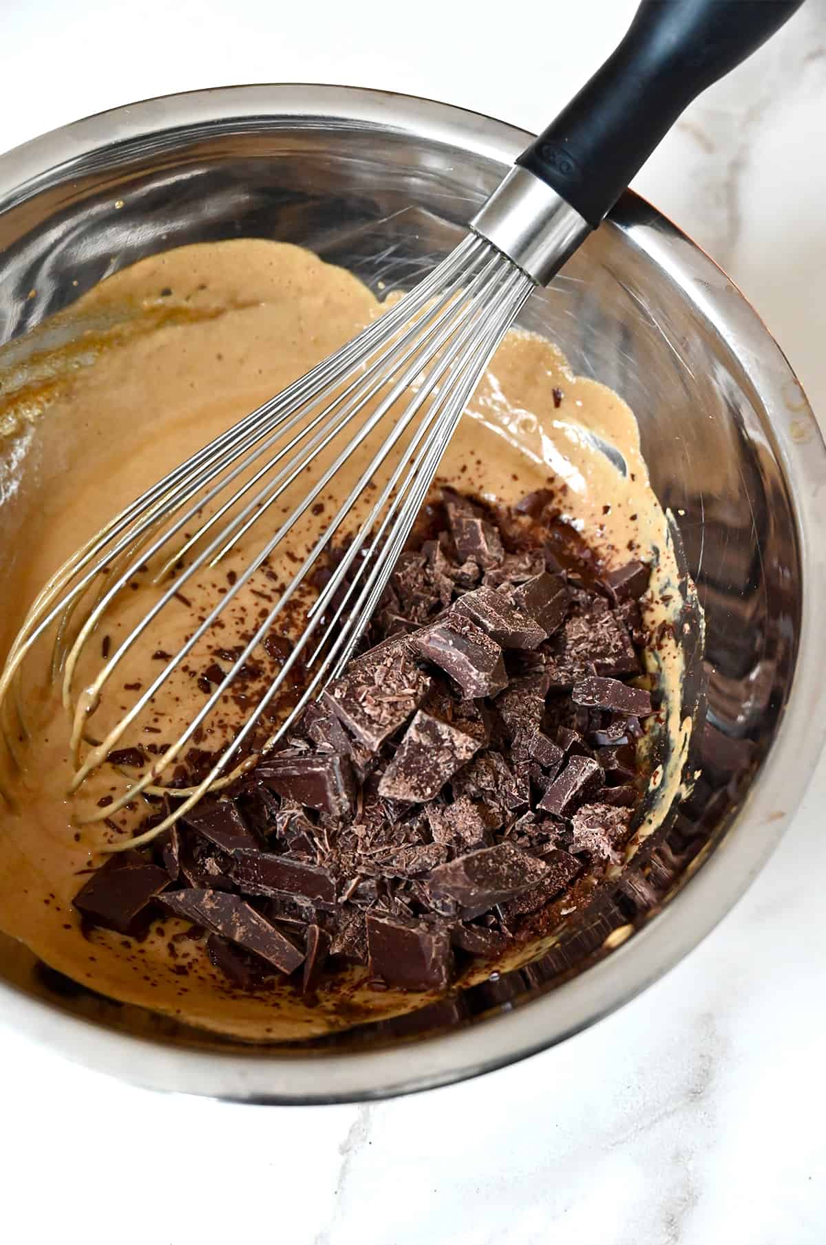 Chopped chocolate being whisked into an egg yolk-espresso mixture in a stainless steel bowl.