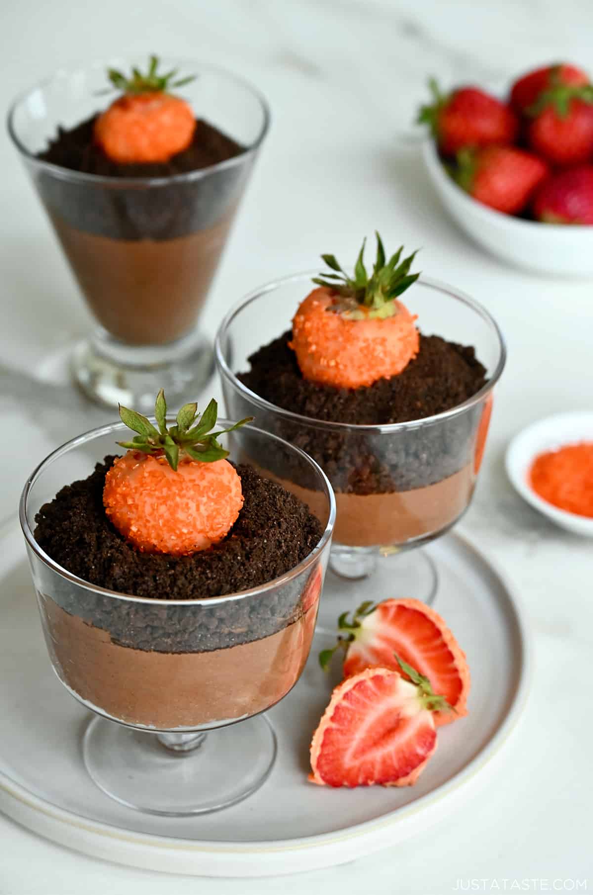 Three chocolate mousse parfaits topped with crushed chocolate wafers and strawberries dipped in orange candy melts.