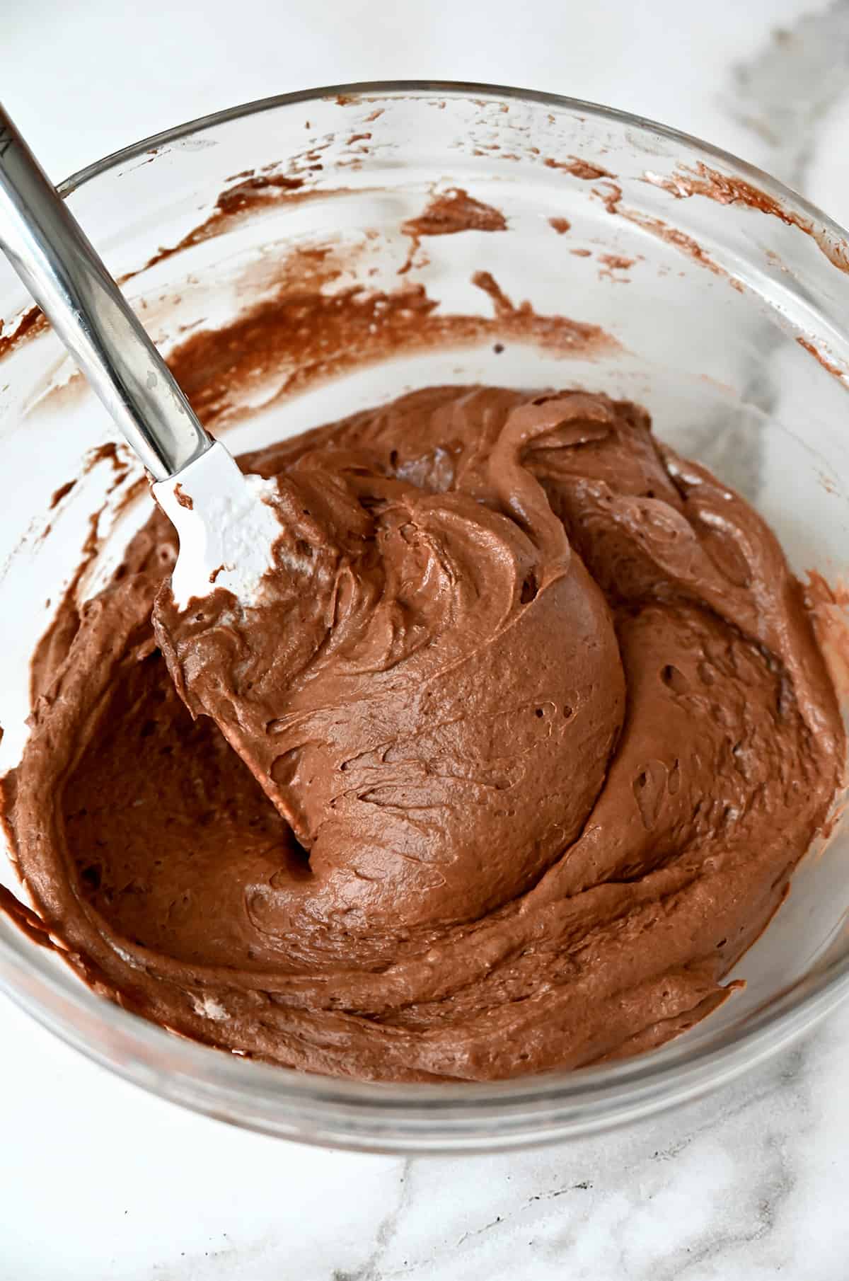Chocolate mousse in a large glass mixing bowl with a rubber spatula propped up against its side.