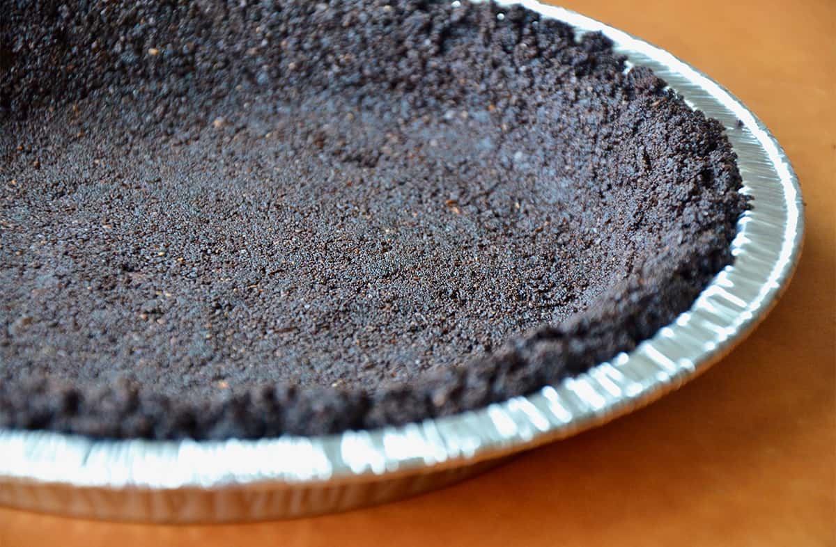 A chocolate cookie pie crust in an aluminum pie tin.