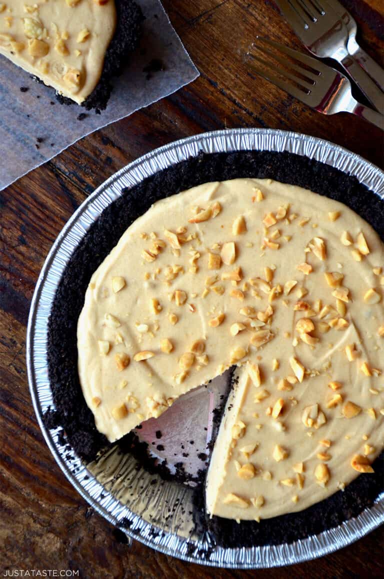 A frozen peanut butter pie topped with chopped peanuts. A slice is taken out of the pie.