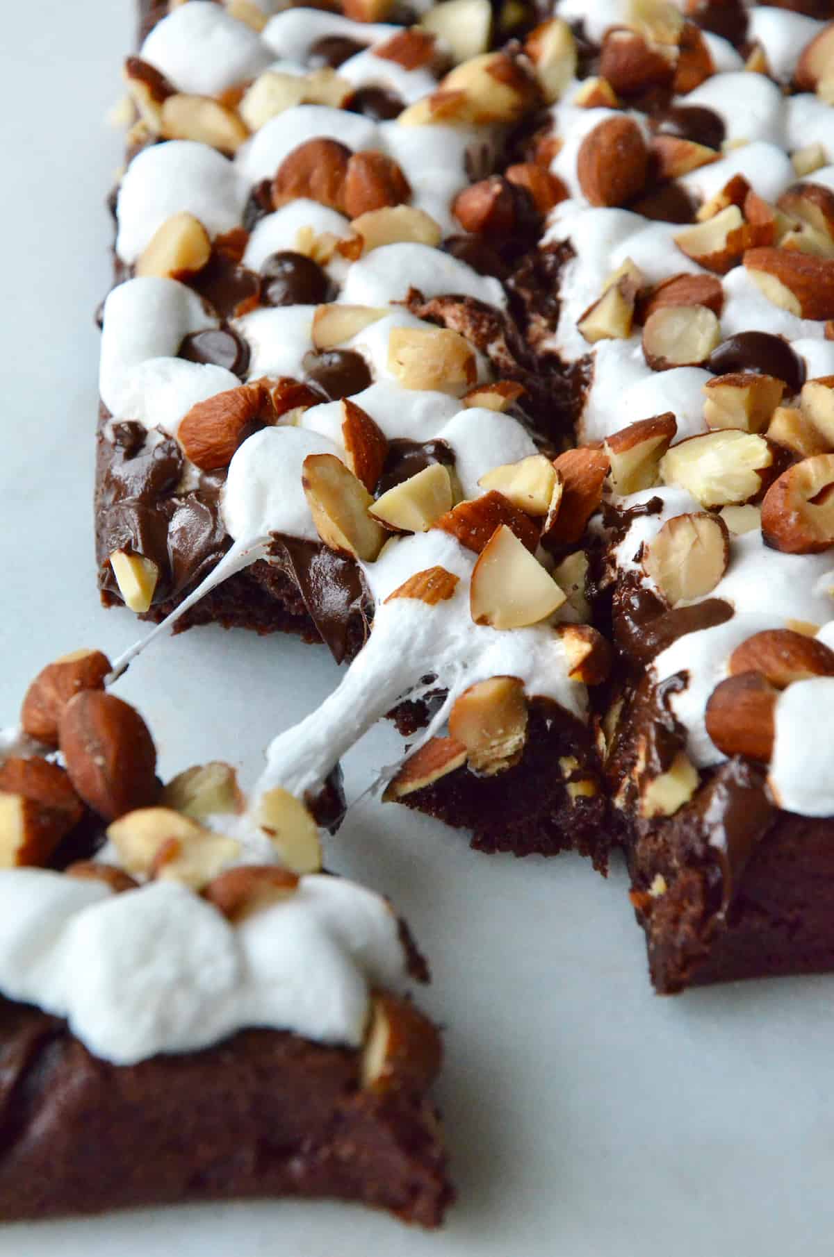 Rock road brownies topped with chopped almonds. A piece of brownie is pulled off the corner.