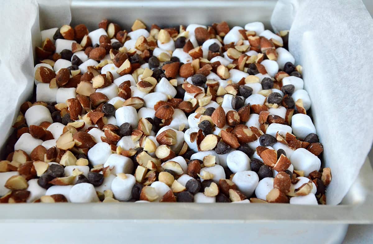 Rock road brownies in a square baking pan topped with chopped almonds, mini marshmallows and chocolate chips.