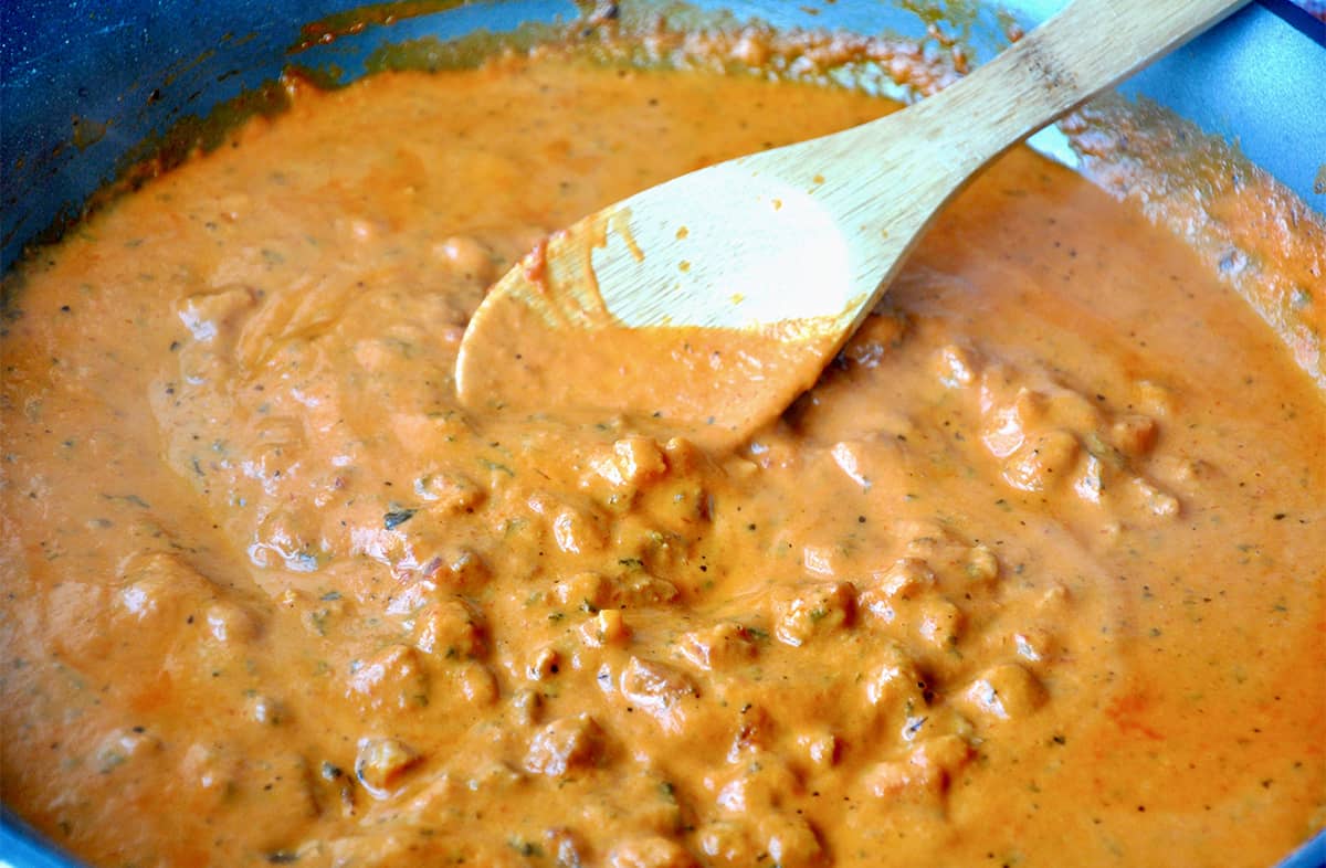A pot of creamy vodka sauce with pancetta is being stirred with a wooden spoon.