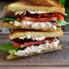 Two halves of a white bread pimento cheese BLT sandwich stacked atop each other.