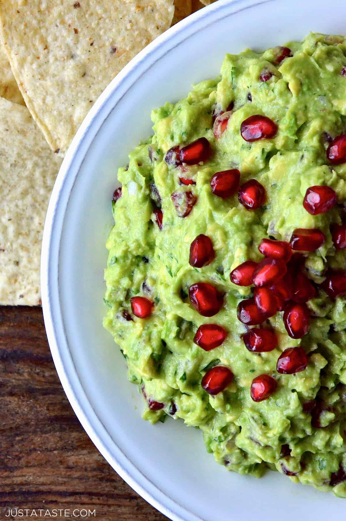 A bowl of pomegranate guacamole topped with extra pomegranate seeds. Tortilla chips are beside the bowl.