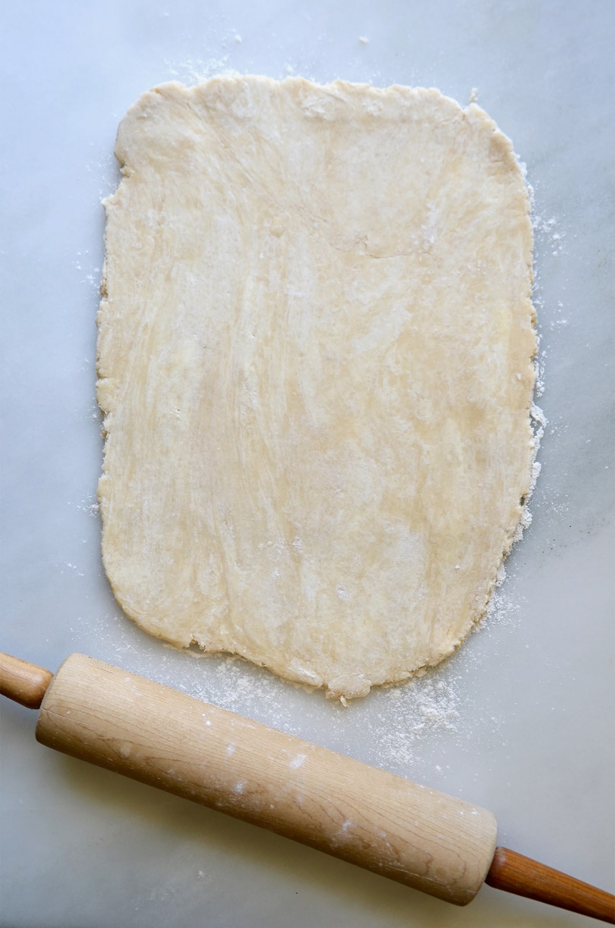 Rolled-out pie dough sits on a white work surface with a wooden rolling pin.