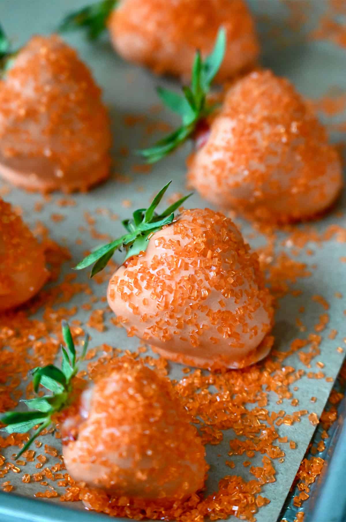 Strawberries dipped in orange candy melts and coated in orange sanding sugar on a parchment-lined baking sheet.