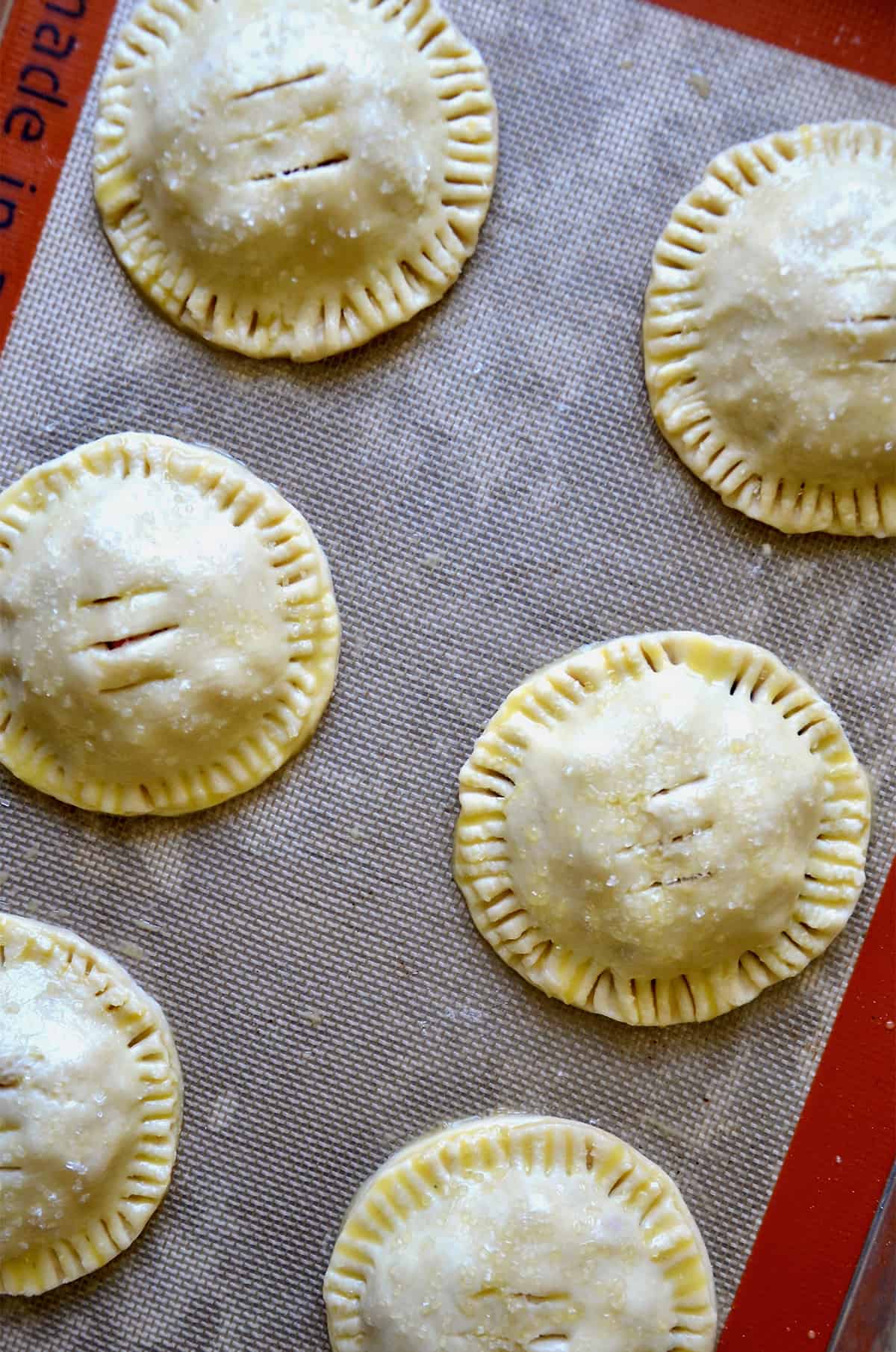 Unbaked hand pies sit on a silicone baking sheet.