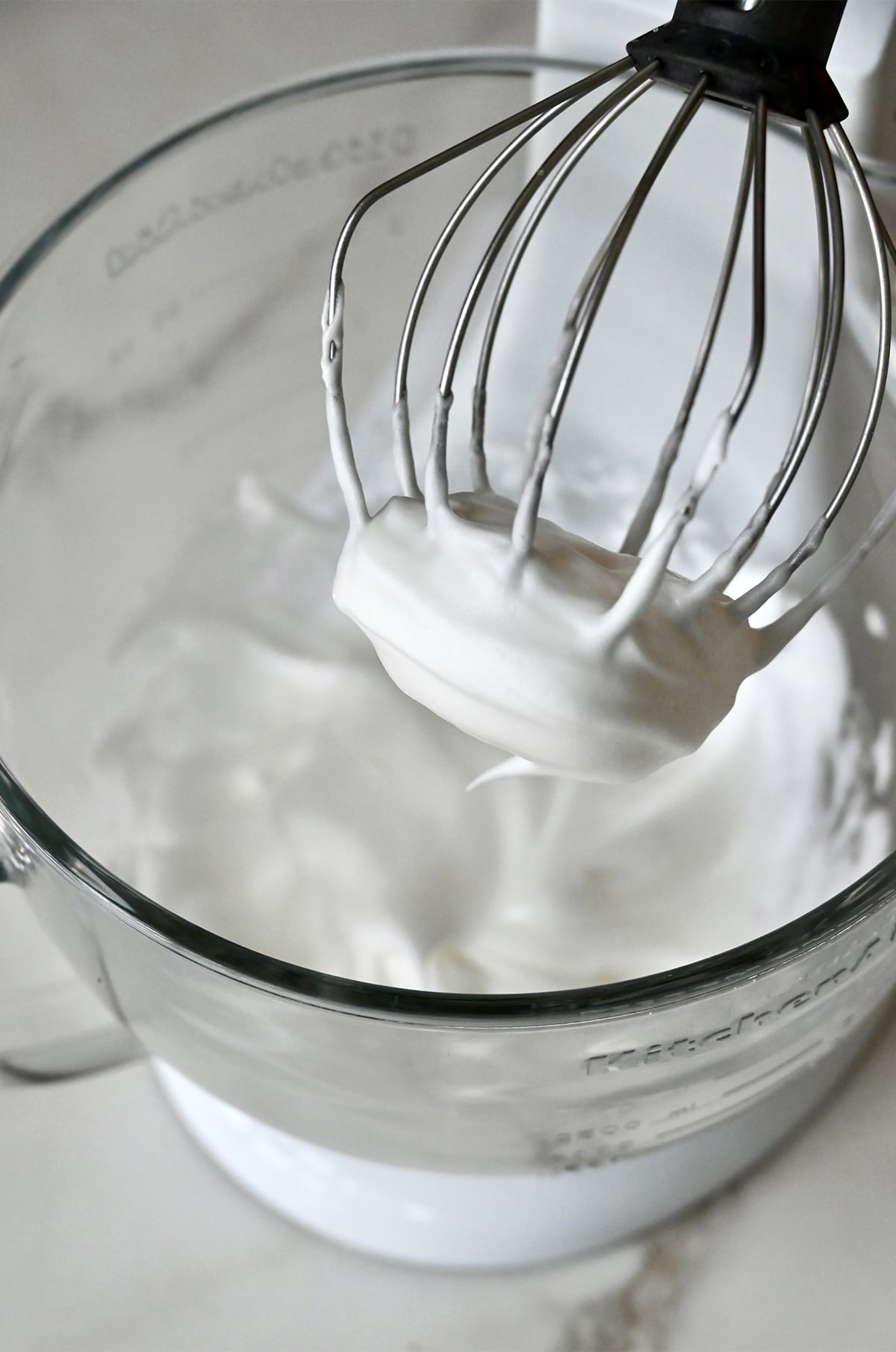 Whipped egg whites in the bowl of a stand mixer fitted with the whisk attachment.