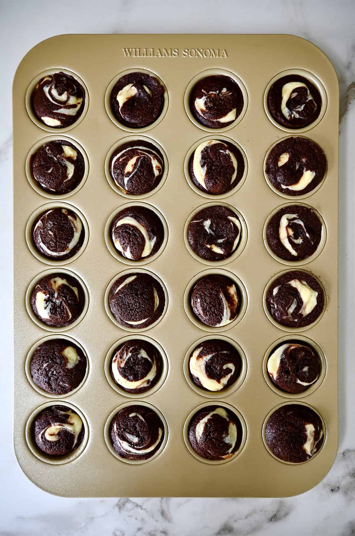 Baked cheesecake brownie bites are in a mini muffin pan.