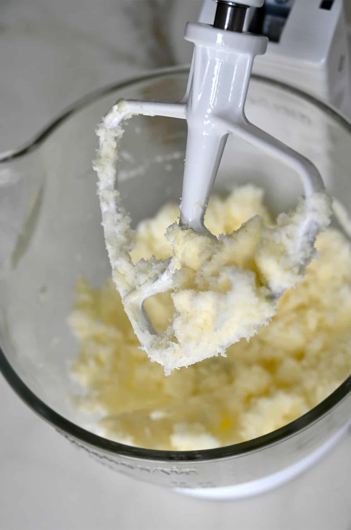 Creamed butter and sugar covering the paddle attachment of a stand mixer bowl.