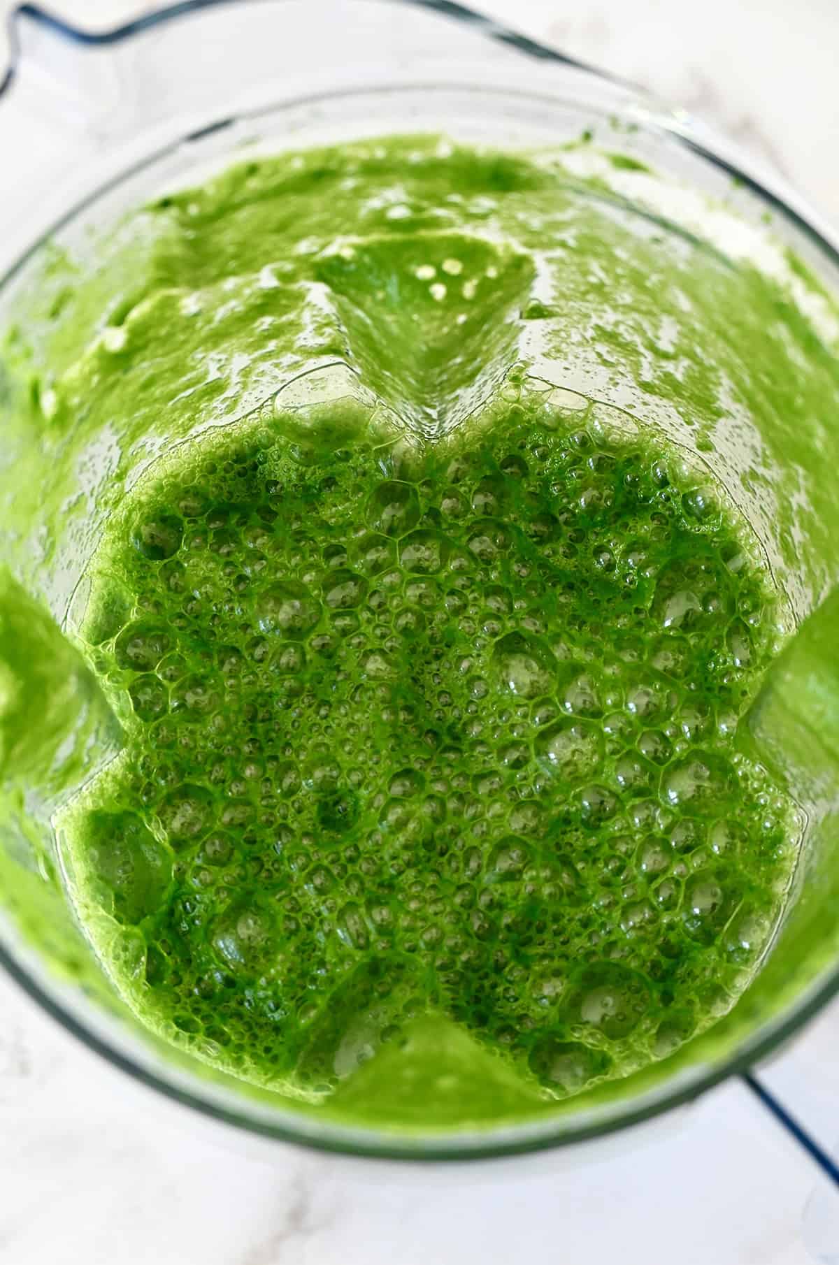 A blender jar is filled with green juice.