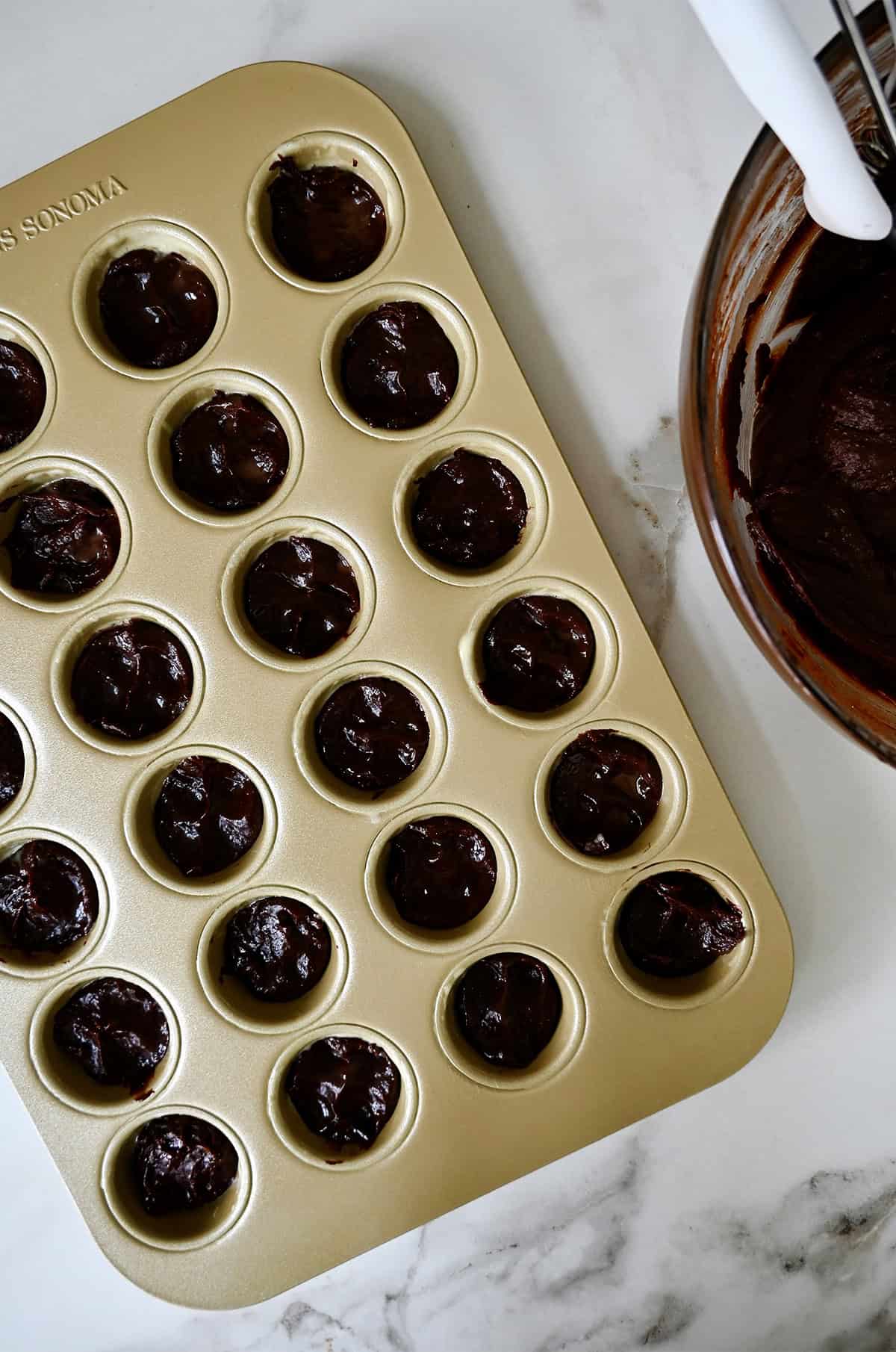 A mini muffin pan is filled with brownie batter.