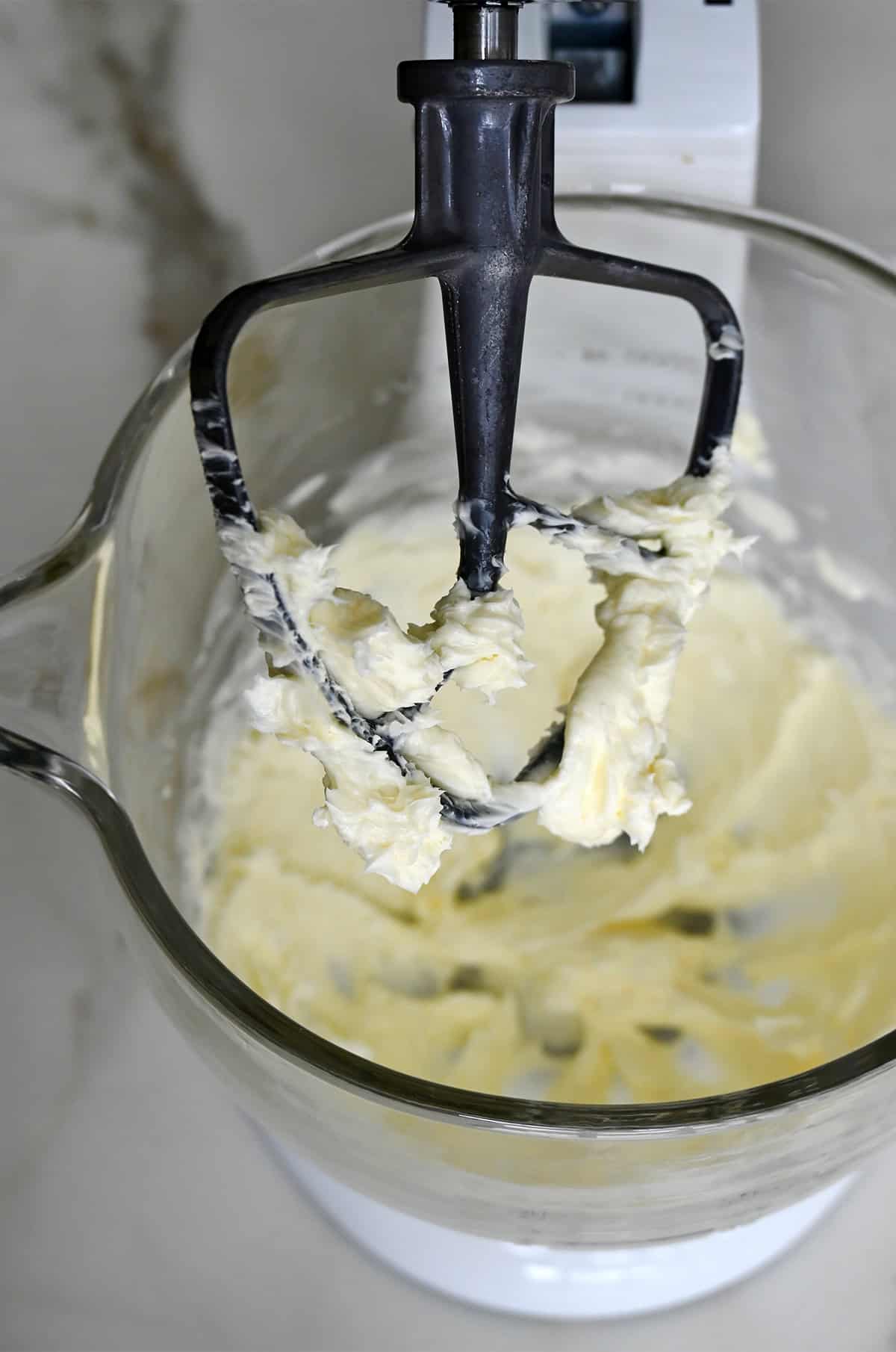 The paddle attachment of a stand mixer covered in whipped butter.