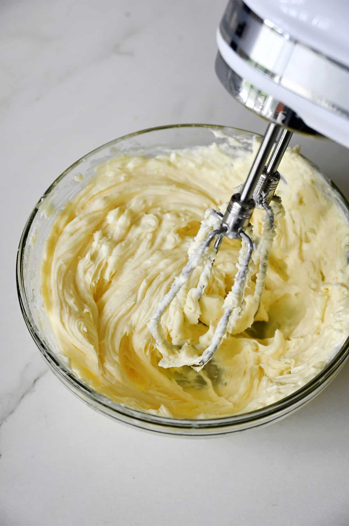 Cheesecake filling in a glass bowl with a hand mixer hovering over the top.