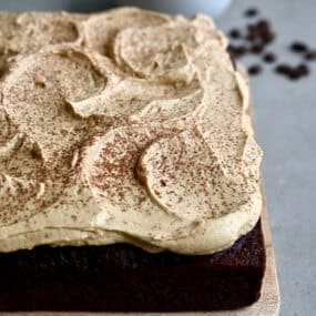A thick layer of coffee buttercream frosting dusted with cocoa powder atop a chocolate sheet cake.