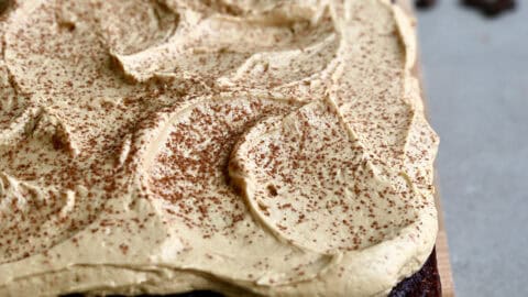 A thick layer of coffee buttercream frosting dusted with cocoa powder atop a chocolate sheet cake.
