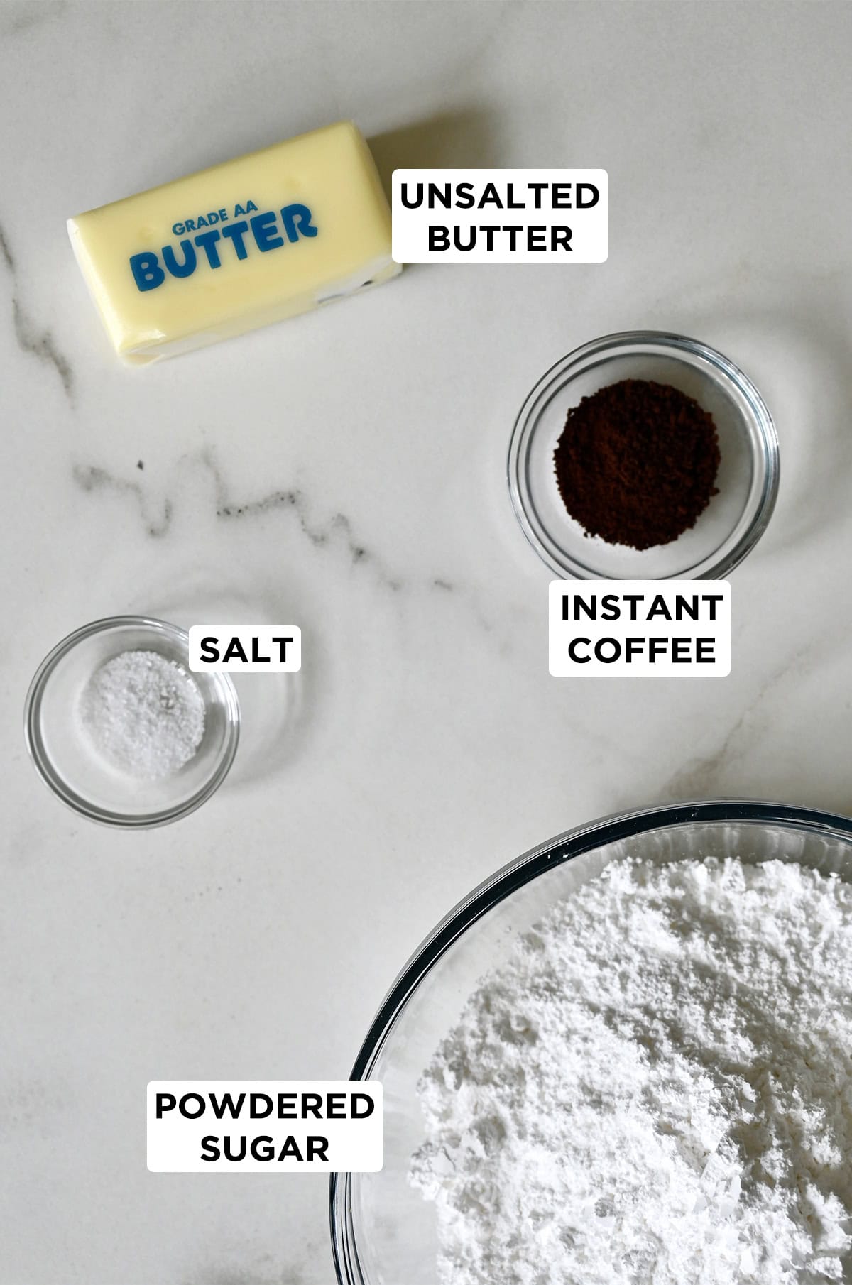 A stick of butter next to a small bowl with instant coffee, a medium bowl with powdered sugar and a small bowl with salt.