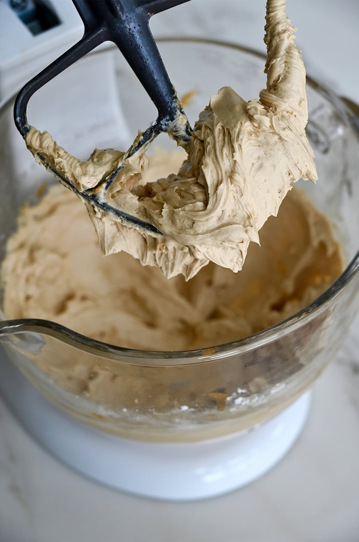 Silky smooth coffee buttercream frosting covering the paddle attachment of a stand mixer.