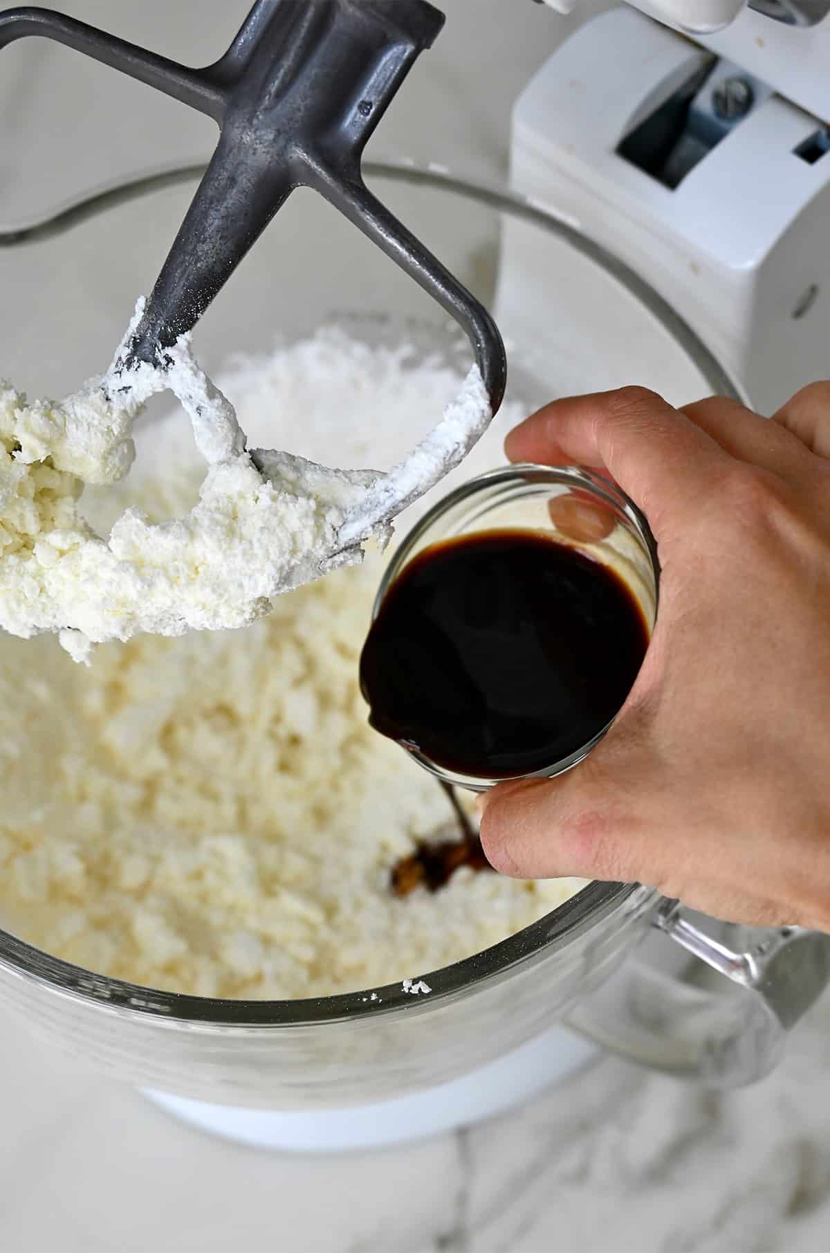 Coffee from a small bowl being poured into the bowl of a stand mixer with buttercream frosting.