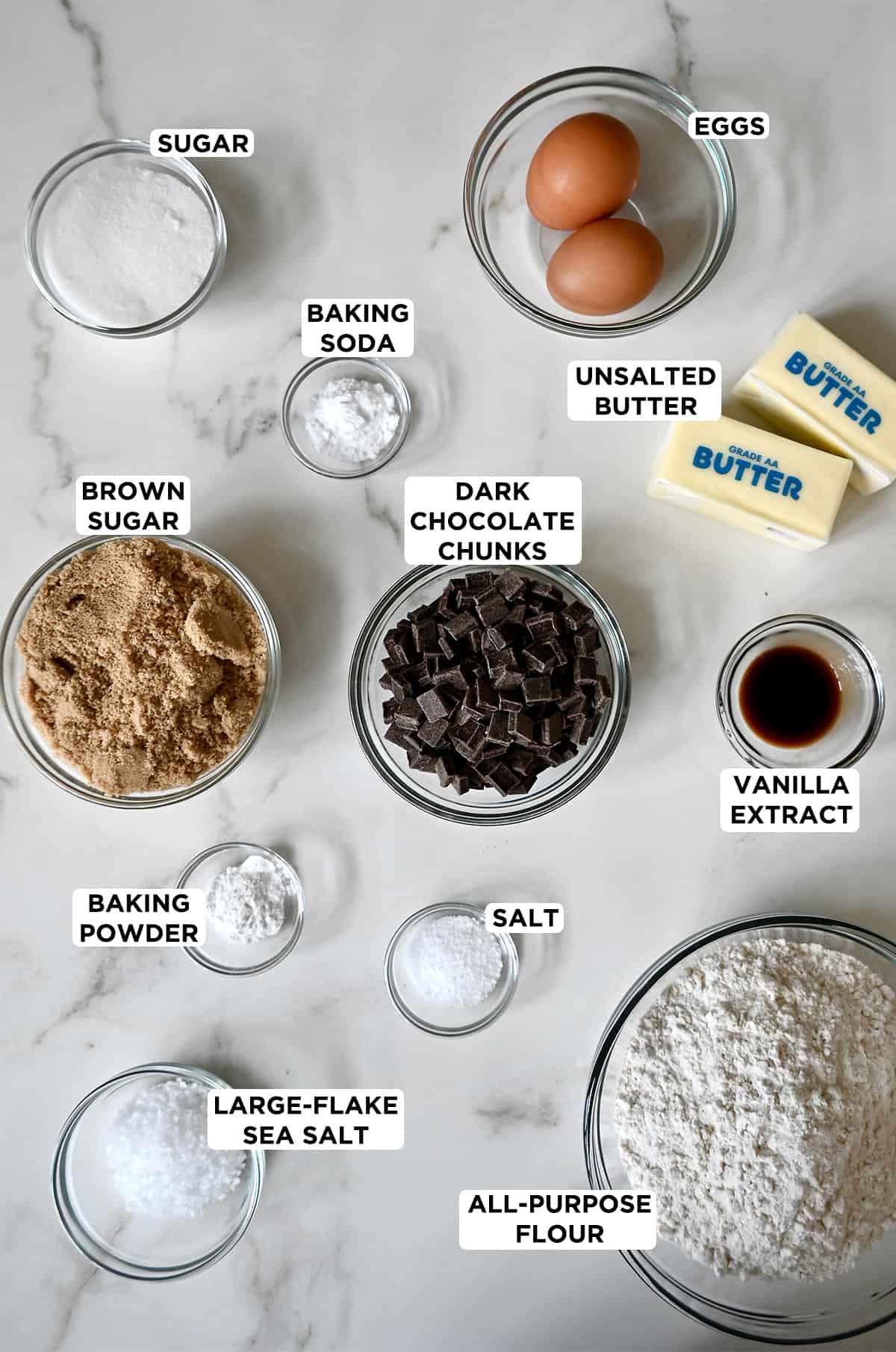 All the ingredients needed to make dark chocolate chunk cookies in various sizes of glass bowls. 