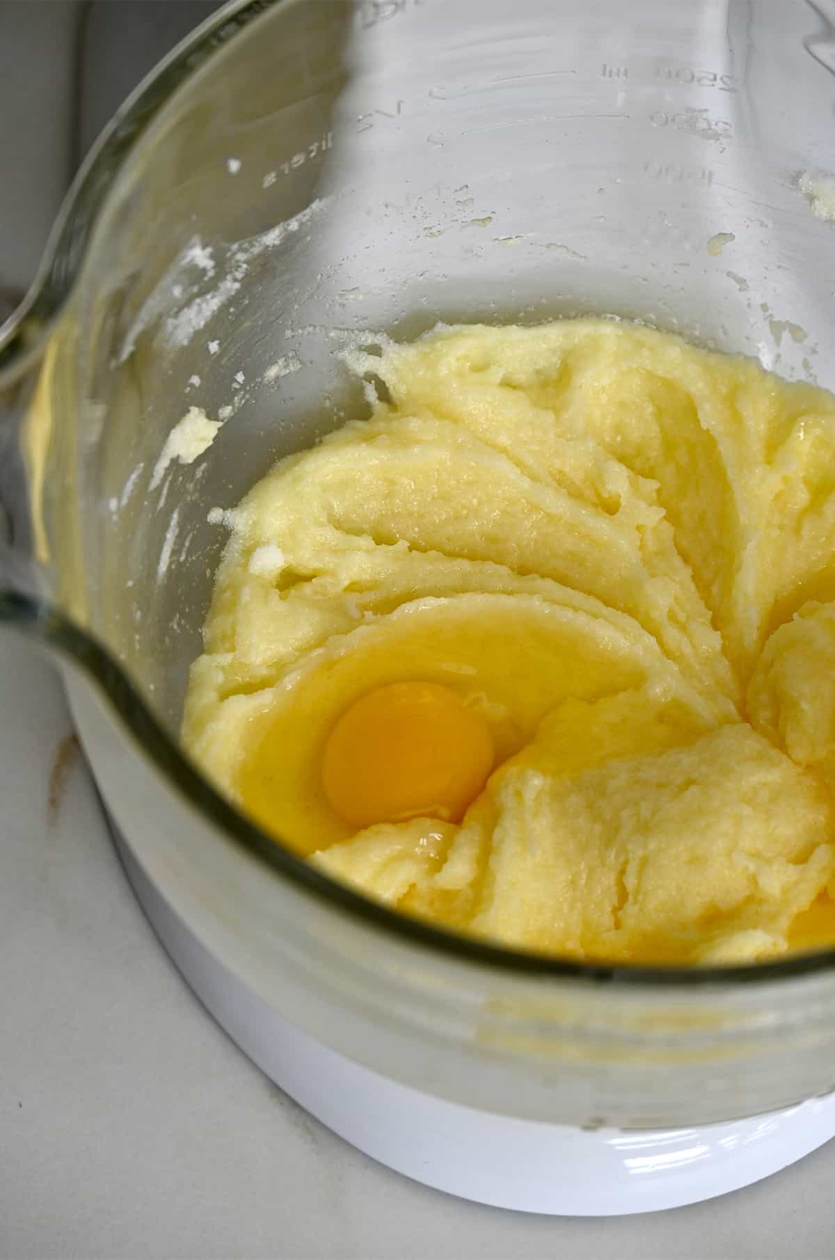 A raw egg atop cake batter in a bowl of a stand mixer. 
