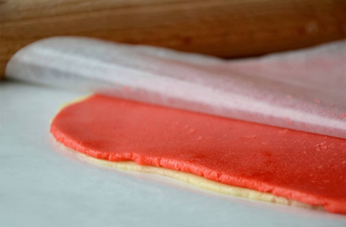 Layers of plain and pink sugar cookie dough is stacked between sheets of wax paper.