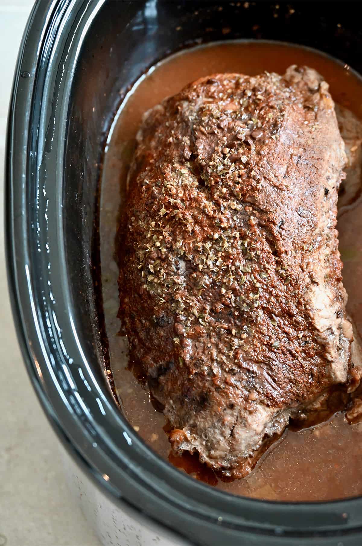 A whole, cooked pork roast in the bowl of a slow cooker.