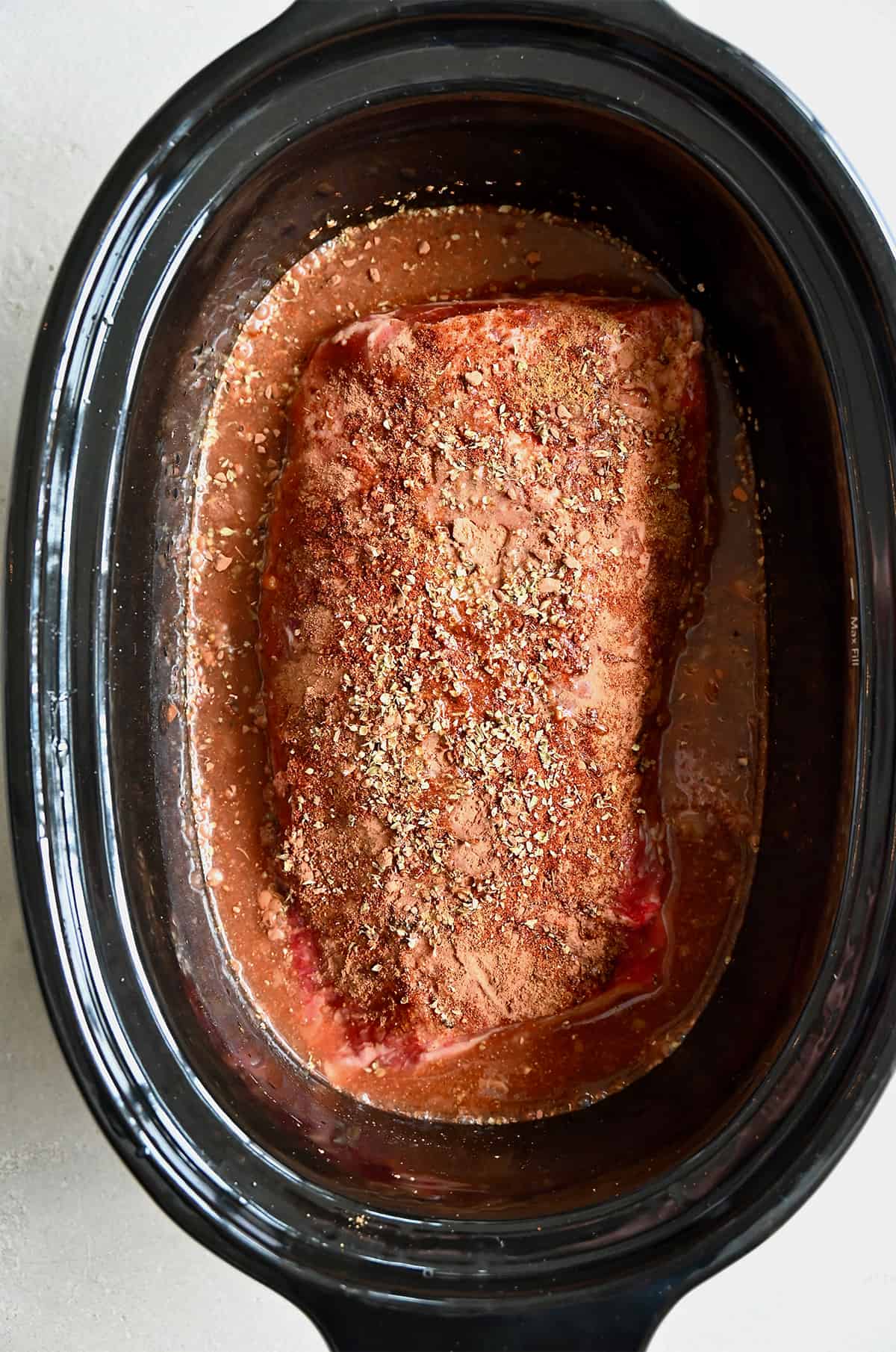 An uncooked pork roast seasoned with spices in the bowl of a slow cooker.