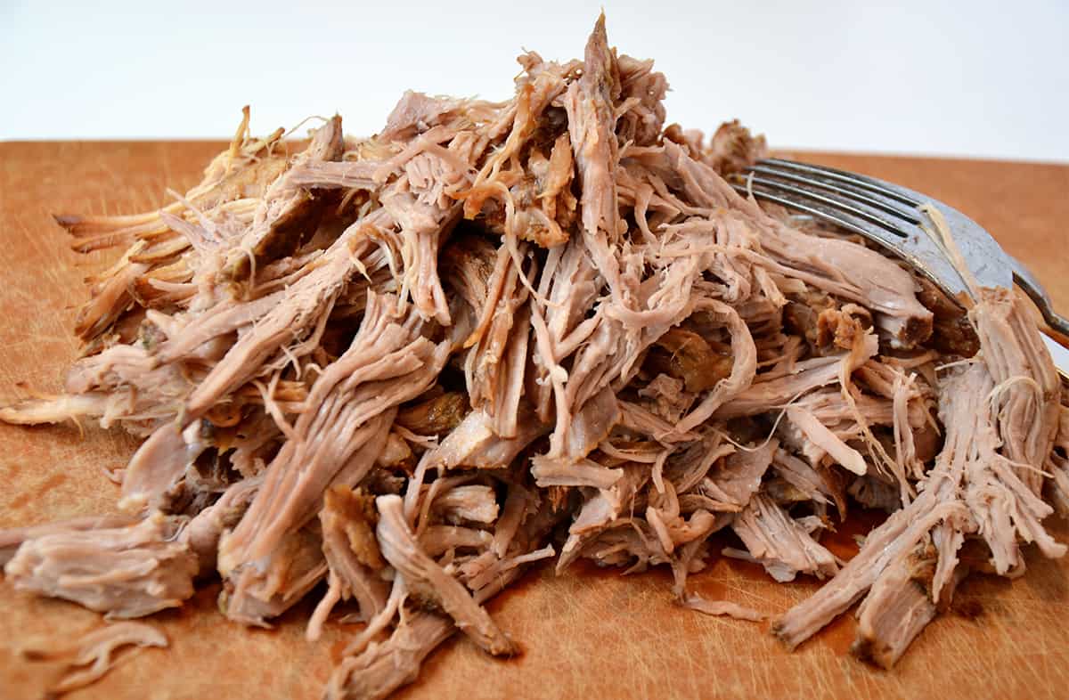 A pile of pulled pork on a cutting board. A fork sits beside the pork.