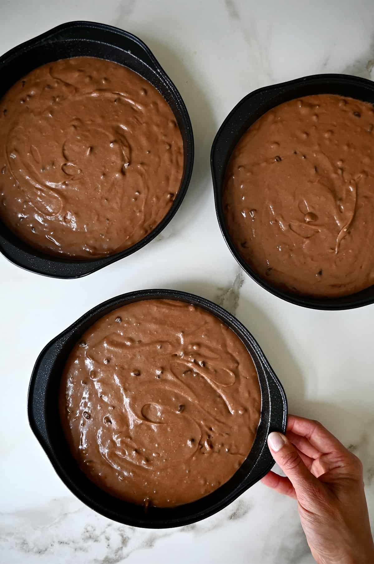 Three round cake pans containing chocolate cake batter.