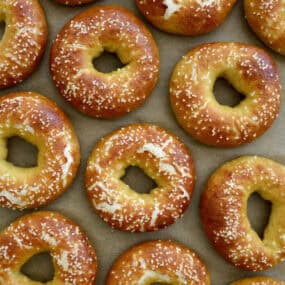 Pretzel bagels topped with kosher salt are arranged on parchment paper.