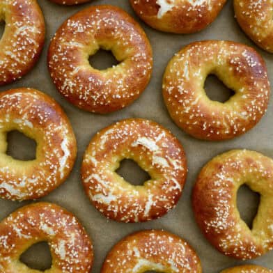 Pretzel bagels topped with kosher salt are arranged on parchment paper.