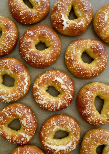 Pretzel bagels topped with kosher salt are arranged on parchment paper.