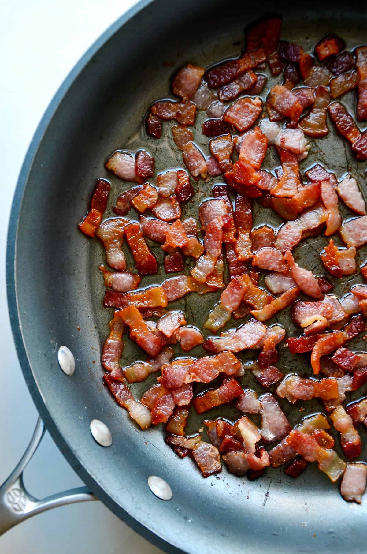 Pieces of bacon cooking in a skillet.