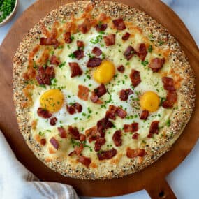 Breakfast pizza topped with eggs, cooked, crispy bacon, sliced chives and everything bagel seasoning.