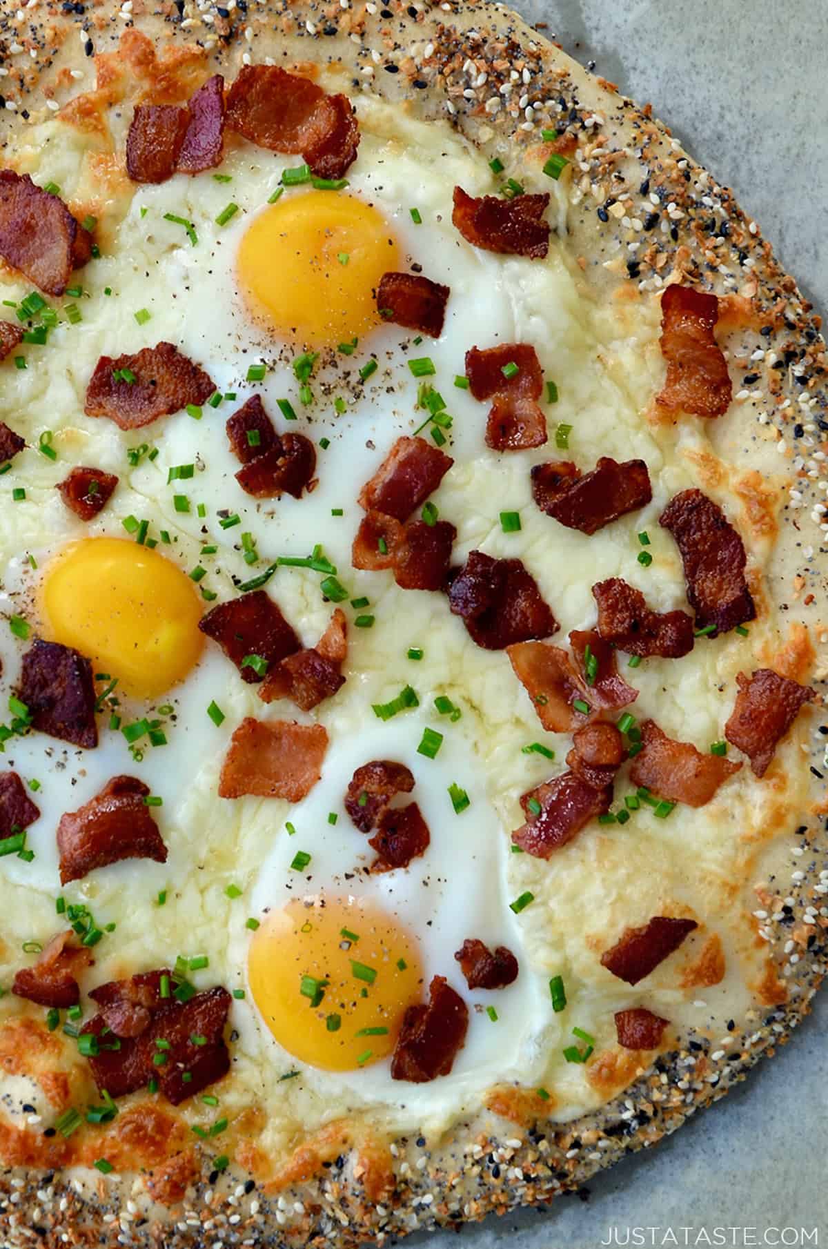 Breakfast pizza topped with eggs, cooked, crispy bacon, sliced chives, everything bagel seasoning and cracked black pepper.