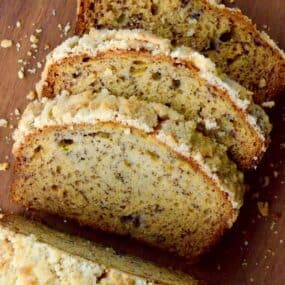 A loaf of banana bread with streusel topping on a wooden cutting board with a couple of slices cut off of it.