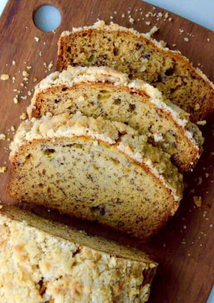 A loaf of banana bread with streusel topping on a wooden cutting board with a couple of slices cut off of it.