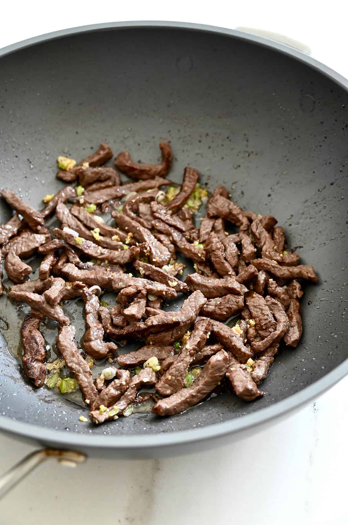 Cooked strips of beef and minced garlic in a wok.